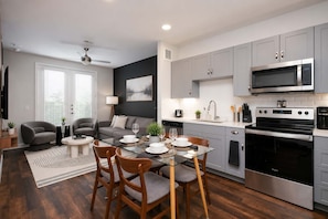 A modern kitchen with stainless steel appliances, a dining area with a glass table, and a living room with a gray sofa and a ceiling fan. - Modern Downtown Retreat with Pool and Gym (San Antonio)