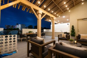 An outdoor patio area with wooden furniture, a dining table, and a view of the cityscape at dusk. - Modern Downtown Retreat with Pool and Gym (San Antonio)