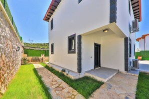 A two-story house with a stone pathway leading to the entrance, a small garden, and a view of the surrounding area. - Villa Çınar-kaş Antalya (Kaş)