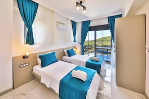 A hotel room with two beds, a balcony with a table and chairs, and a view of the landscape. - Villa Çınar-kaş Antalya (Kaş)