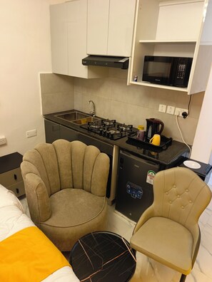 A compact kitchenette with a gas stove, microwave, and a small refrigerator. There is a chair and a bed in the room. - Cozy Studio apartment near JKI Airport and SGR in Nairobi perfect for your stay (Nairobi)