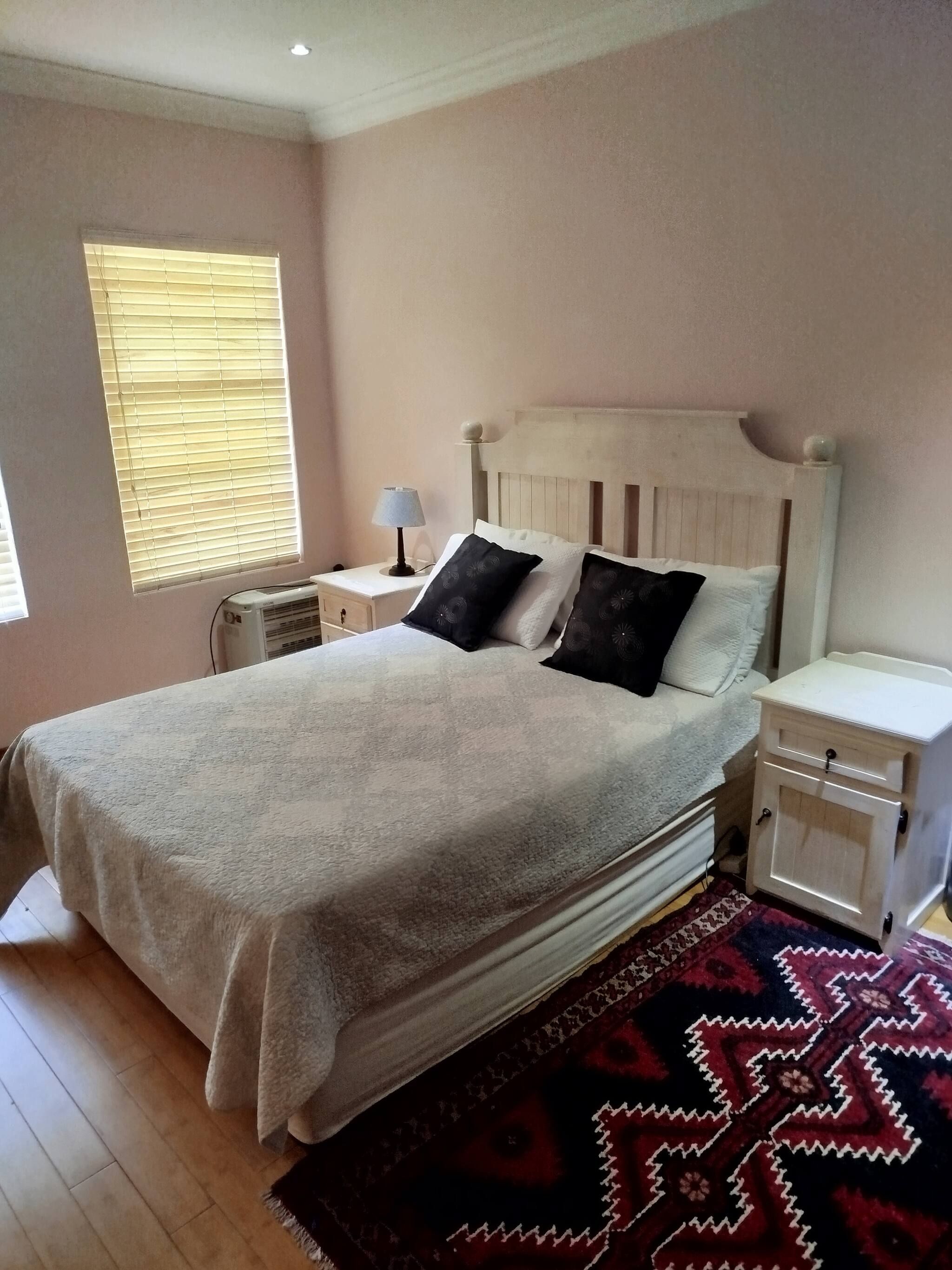 Un dormitorio con cama, mesitas de noche, lámpara y ventana con persianas.