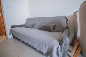 Ein graues Sofa mit strukturierter Bezüge und zwei Kissen, platziert vor einer schlichten Wand mit einer Tür und Lichtschalter.