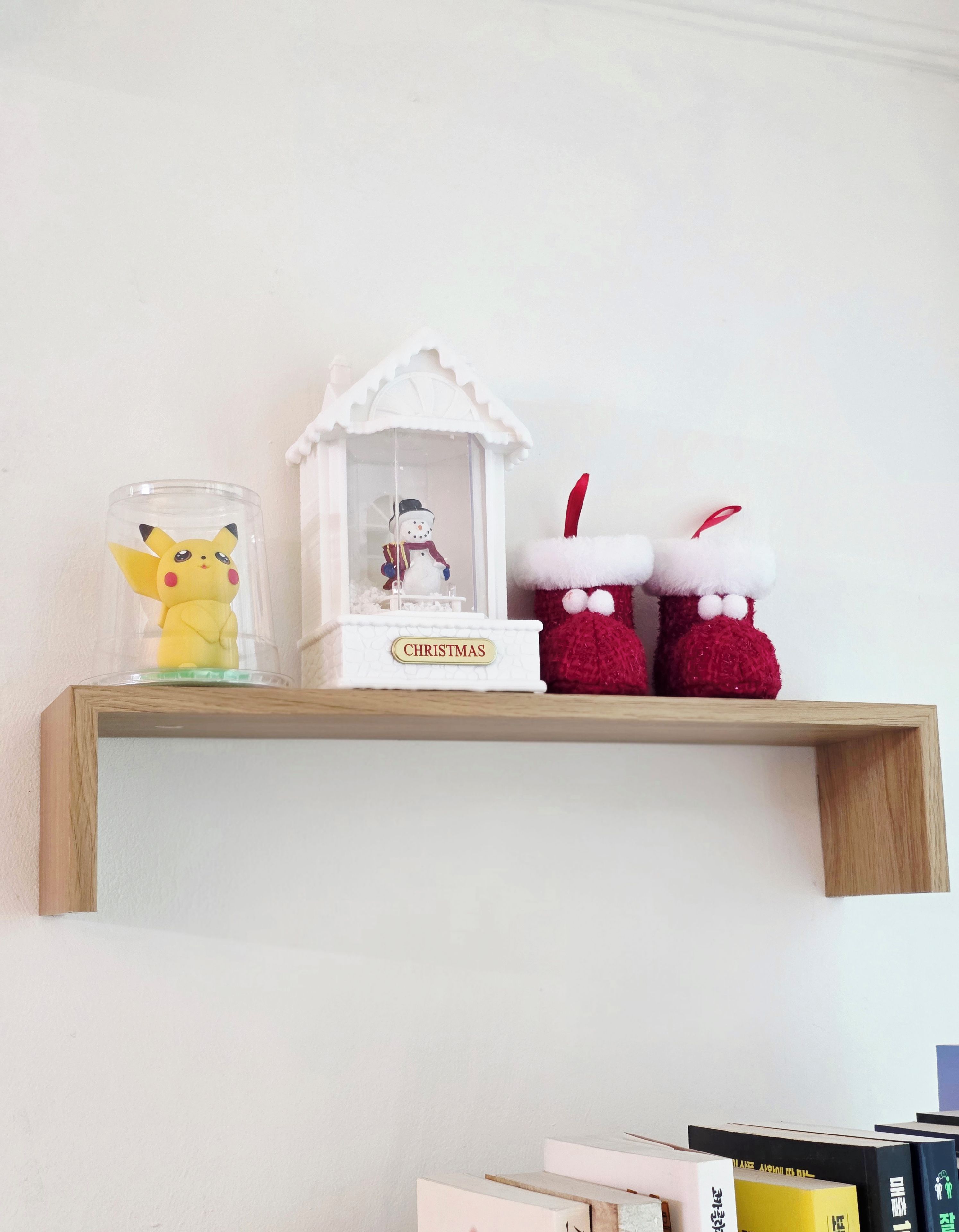 Ein hölzernes Regal mit einem Glasbehälter, der eine Pikachu-Figur, eine Schneemann-Figur und zwei rote Weihnachtsmänner-Ornamente enthält.