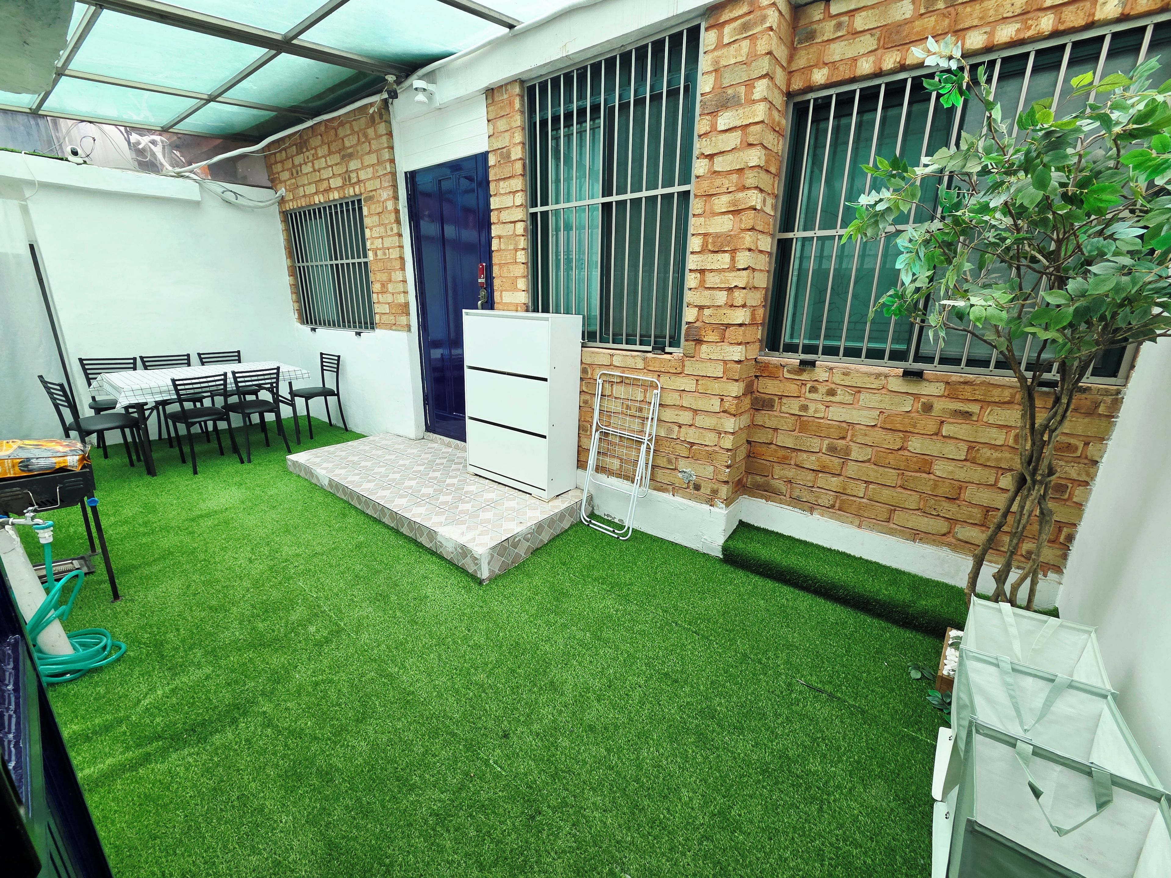 A small courtyard with artificial grass, a white cabinet, and a table with chairs.