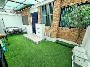 A small courtyard with artificial grass, a white cabinet, and a table with chairs.