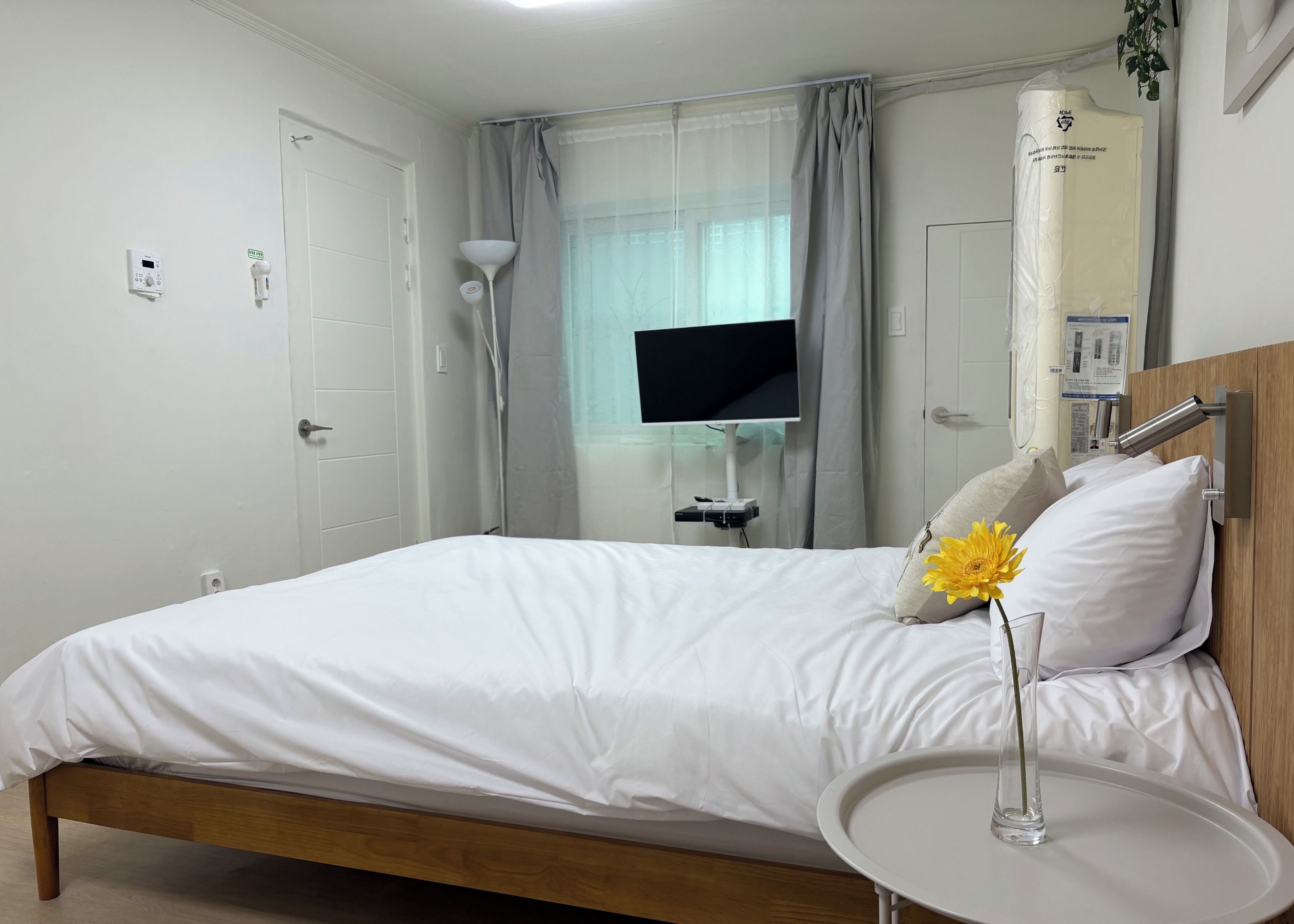 Ein Hotelzimmer mit einem Bett, einem Nachttisch mit einer Vase, einem Fernseher und einem Fenster mit Vorhängen.