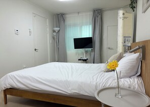 Een hotelkamer met een bed, een nachtkastje met een vaas, een televisie en een raam met gordijnen.
