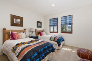 A bedroom with two beds, a nightstand, a lamp, and two windows with patterned curtains. - Mediterranean style retreat. (Solana Beach)