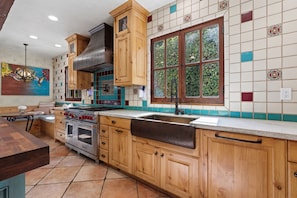 A kitchen with wooden cabinets, a stove, and a window with a view of greenery. - Mediterranean style retreat. (Solana Beach)