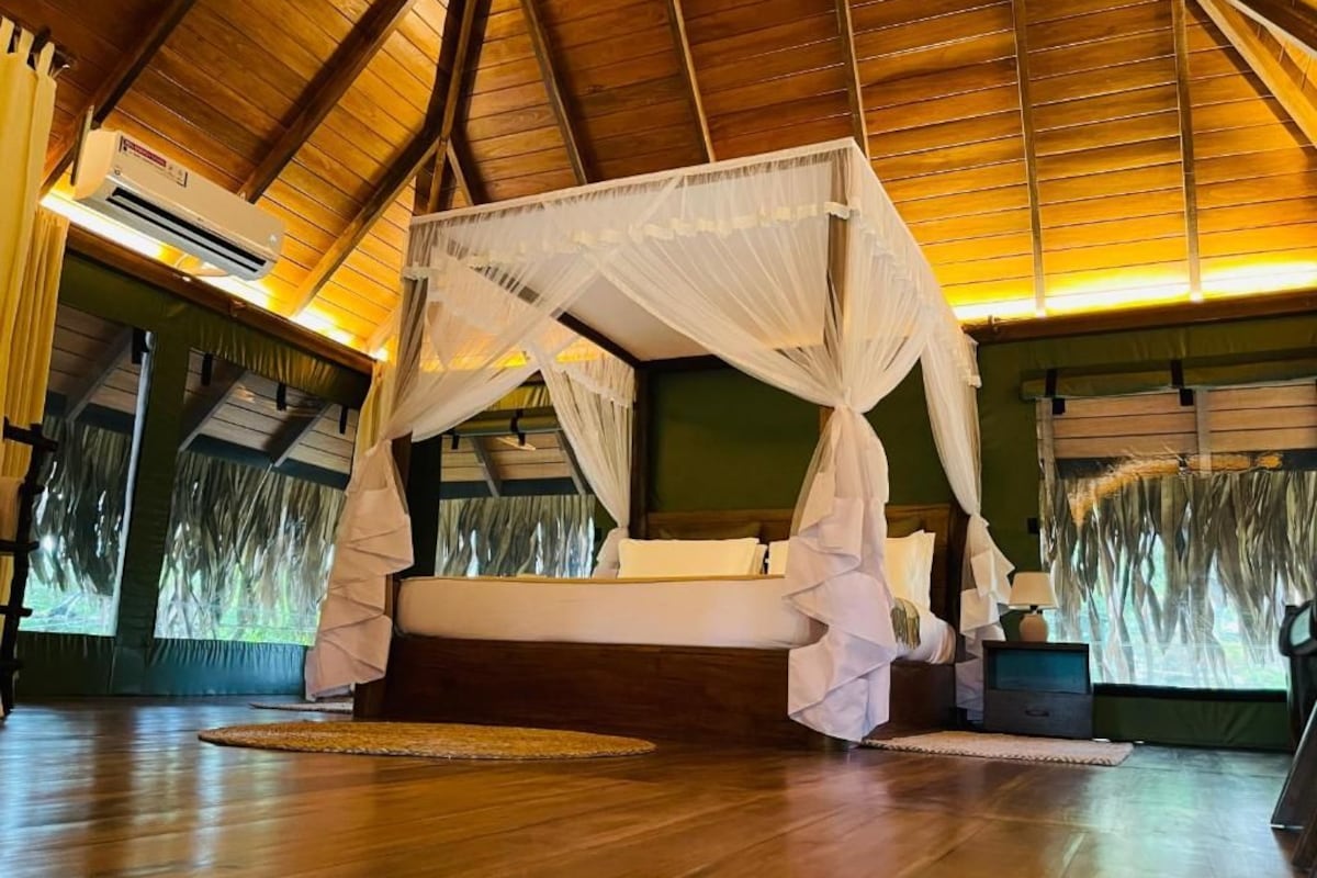 Een kamer met een hemelbed, een houten plafond en uitzicht door het raam.