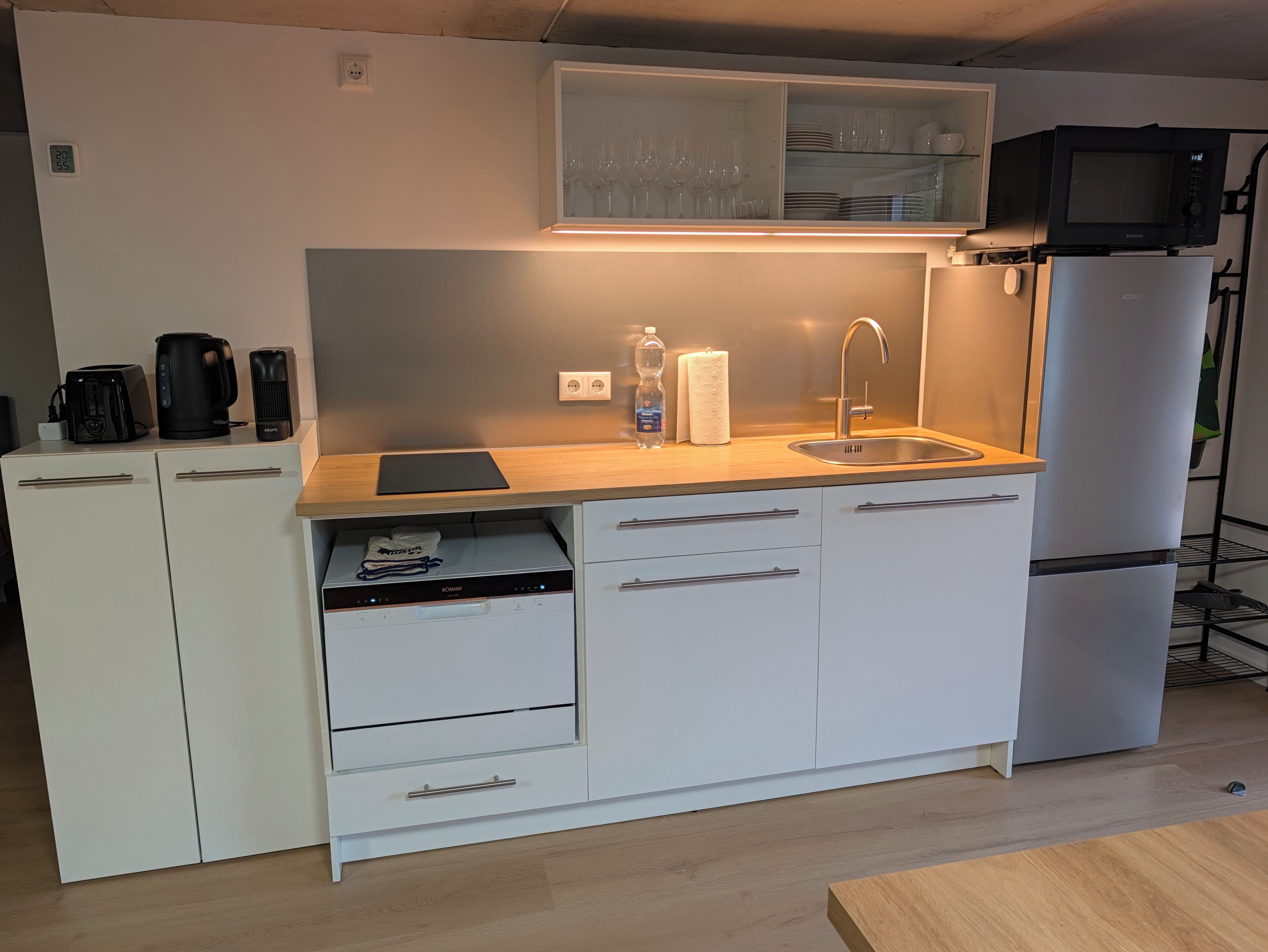 A compact kitchenette with a microwave, toaster, and coffee maker on the countertop, a sink, and a refrigerator.