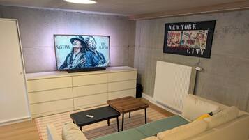 En stue med en hvid sofa, et sofabord, et fjernsyn på et stativ og et billede på væggen.