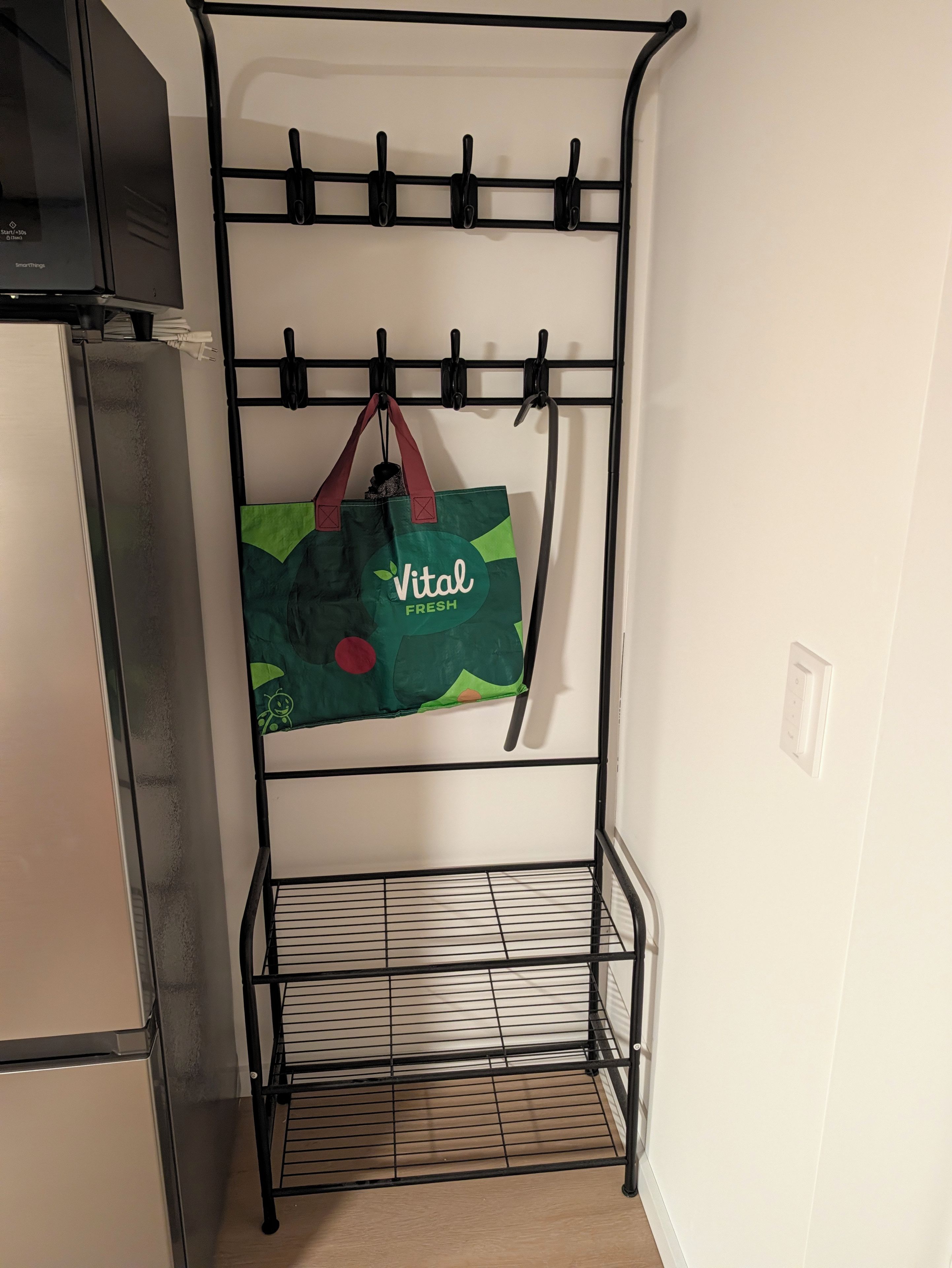 A metal rack with hooks, a green bag hanging, and a tiled floor.