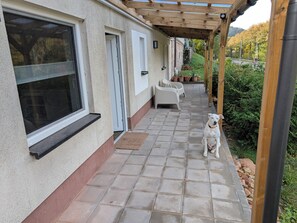 A covered patio with a tiled floor, a white dog, and outdoor furniture.