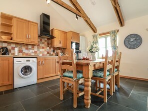 A kitchen with wooden cabinets, a Bosch washing machine, a dining table with chairs, and a clock on the wall. - Ash Cottage (Truro)