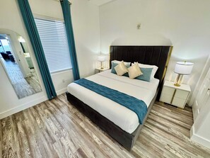 A hotel room with a large bed, two bedside tables with lamps, a mirror, and a window with curtains. - Balcony Lake Views | Pool, Gym, WiFi & Parking (Orlando)