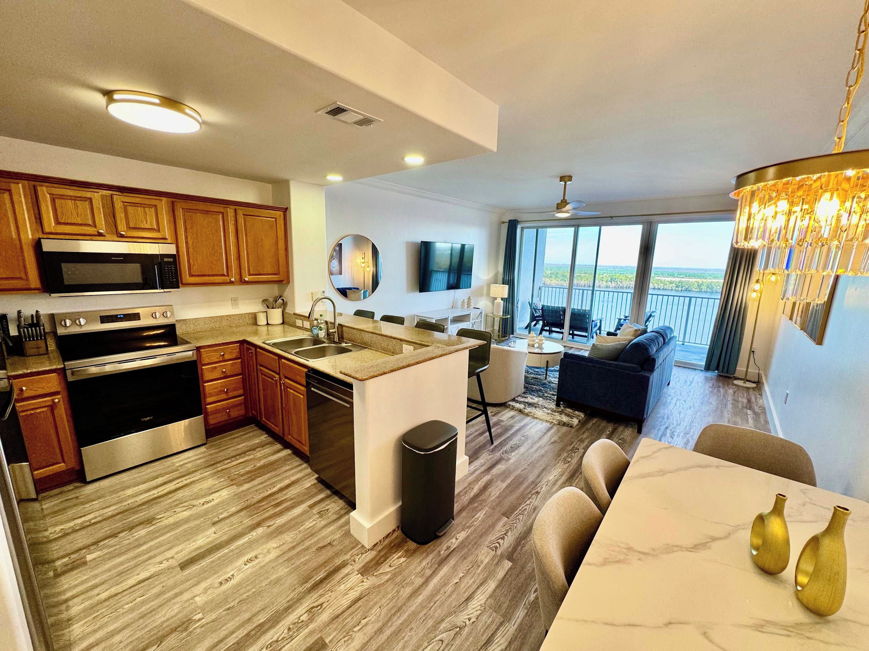 A modern kitchen with stainless steel appliances, a dining area with a marble table, and a balcony with a view.