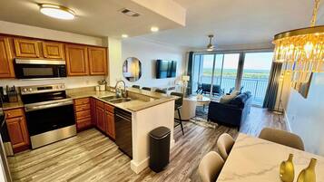A modern kitchen with stainless steel appliances, a dining area with a marble table, and a balcony with a view.