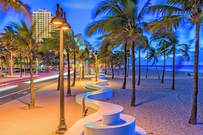 A beachside promenade with palm trees, a curved pathway, and a street with light trails. - The Beachside Escape I New Pool & Spa! (Hollywood)