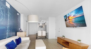 A modern living room with a large flat-screen TV, a white sofa with blue cushions, a wooden console table, and a map on the wall. - 1 BR APT Resort Style - Resort Amenities (Hallandale Beach)