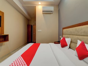 Ein Hotelzimmer mit Bett, Kissen, Nachttisch, Klimaanlage und einem Holzschrank.