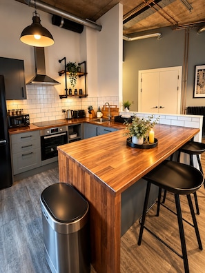 A modern kitchen with a wooden island, stainless steel appliances, and a hanging light fixture. - Luxury 2BR Wembley Loft | Skyline Views | Near Wembley Stadium (Wembley)