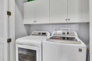 Una sala de bugaderia amb dues rentadores blanques de càrrega frontal i un armari a la part superior.