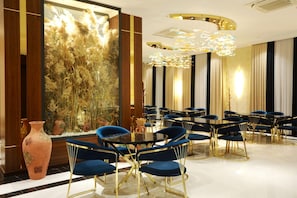 A modern dining area with round tables and blue chairs, a decorative wall with tall plants, and a large vase. - Ramada by Wyndham (Nukus)