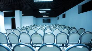A conference room with rows of chairs, a projector screen, and a ceiling with grid-like pattern and lights.
