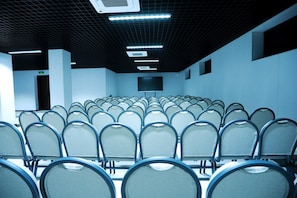 A conference room with rows of chairs, a projector screen, and a ceiling with grid-like pattern and lights. - Ramada by Wyndham (Nukus)