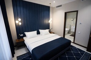 A hotel room with a large bed, bedside tables, a mirror, and a bathroom visible through an open door. - Ramada by Wyndham (Nukus)
