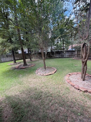 A backyard with multiple trees, a wooden fence, and a grassy lawn. - Panther Creek Retreat - Heart of The Woodlands (Spring)
