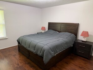 Un dormitorio con una cama de madera, dos mesitas de noche con lámparas y una ventana con persianas.