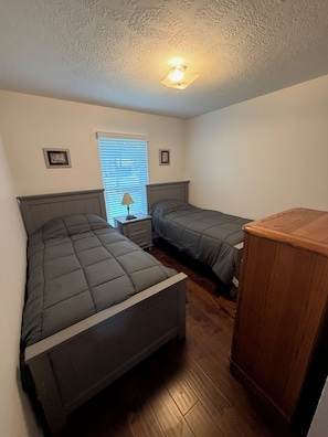 A bedroom with two beds, a nightstand, a lamp, and a wooden cabinet. - Panther Creek Retreat - Heart of The Woodlands (Spring)