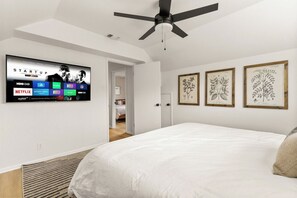 A bedroom with a bed, a ceiling fan, a mounted TV displaying streaming services, and framed botanical prints on the wall. - Not My First Rodeo | Pool & Spa | Game Room (San Antonio)
