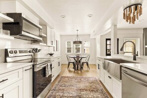 Une cuisine moderne avec des meubles blancs, une cuisinière en acier inoxydable et un coin repas agrémenté d’un tapis à motifs.