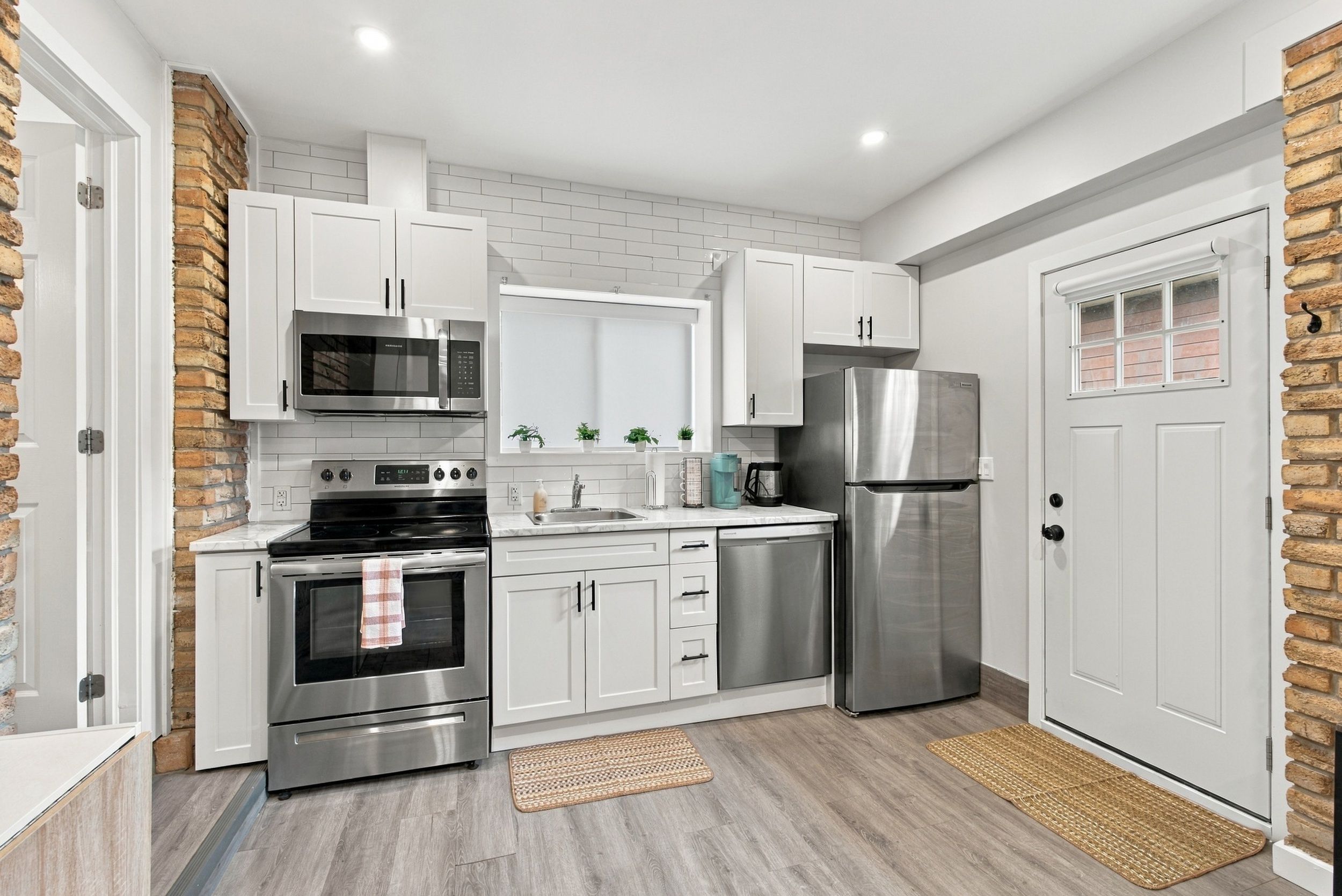 A modern kitchen with white cabinets, stainless steel appliances, and a brick accent wall.