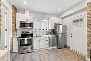 A modern kitchen with white cabinets, stainless steel appliances, and a brick accent wall. - The Chic Studio in Niagara College (Welland)