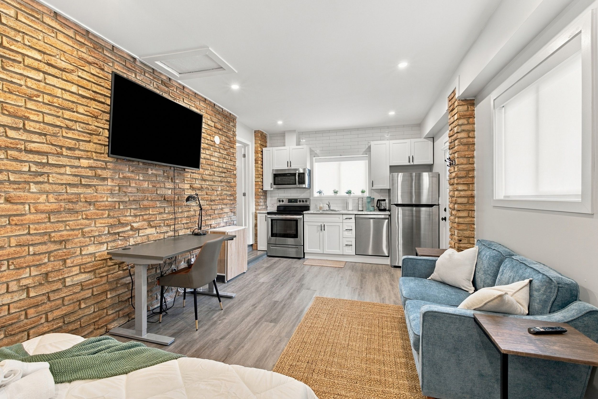 A modern kitchen with white cabinets, stainless steel appliances, and a brick accent wall.