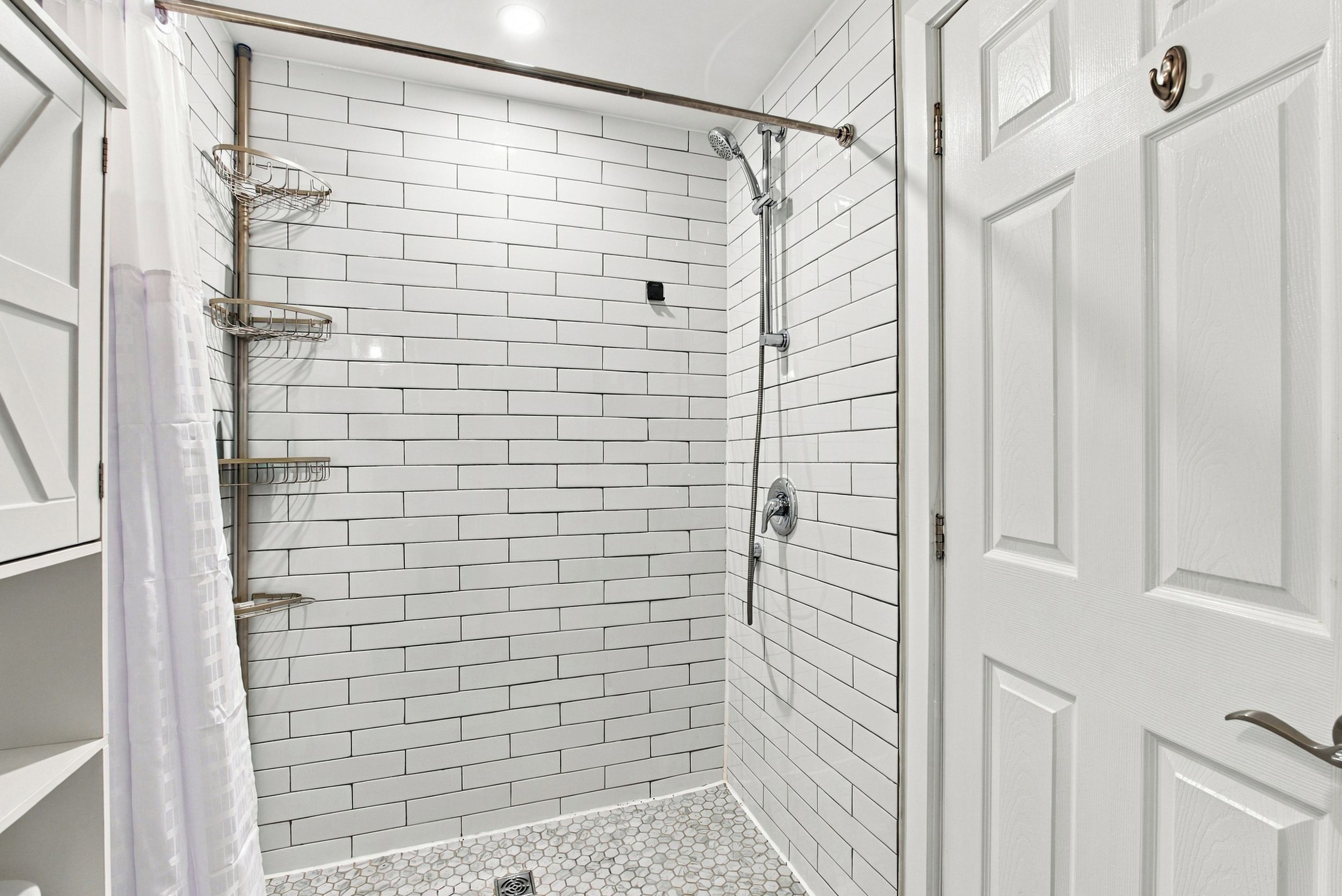 Ducha en esquina con azulejos tipo metro blancos, puerta de cristal y cabezal metálico.