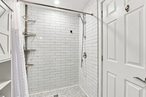 A corner shower with white subway tiles, a glass shower door, and a metal showerhead. - The Chic Studio in Niagara College (Welland)