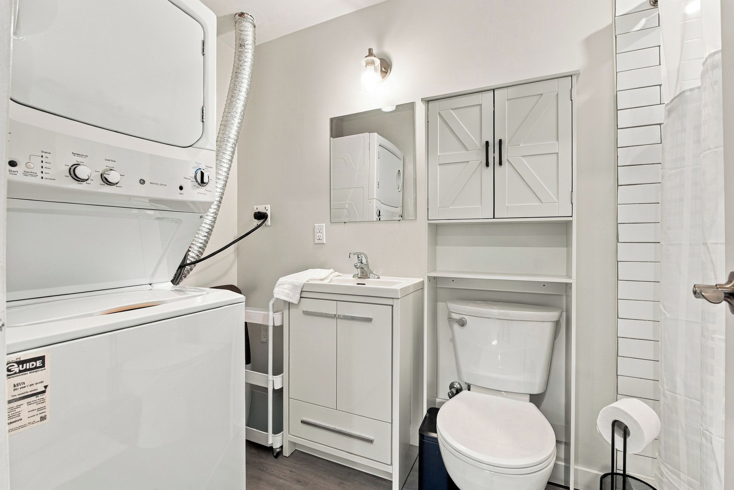 A compact, modern bathroom with a built-in washer and dryer, a sink, a toilet, and a mirror.
