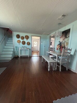 Une pièce spacieuse avec un plancher en bois, une table à manger avec des chaises, un escalier et une porte donnant sur une autre pièce.