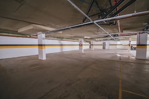 An underground parking garage with concrete pillars, yellow and black striped walls, and overhead pipes. - Nixxus 216 (Ipojuca)