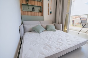Un lit avec un matelas matelassé, deux oreillers et une tête de lit adossée à un mur sur lequel se trouve une étagère.