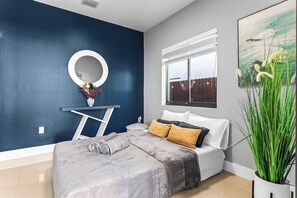 A bedroom with a bed, a round mirror, a window, and a plant. - Sunset Villa | Pool ·BBQ ·Outdoor kitchen & Grill (Hialeah)