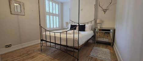 A bedroom with a four-poster bed, a bedside table with a lamp, and a deer skull decoration on the wall.
