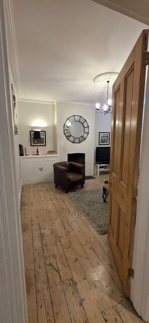 Una habitación con piso de madera, un sillón de cuero marrón, un espejo redondo en la pared y una puerta a la derecha.