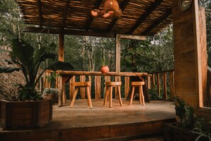 An outdoor wooden deck with a thatched roof, surrounded by lush greenery.